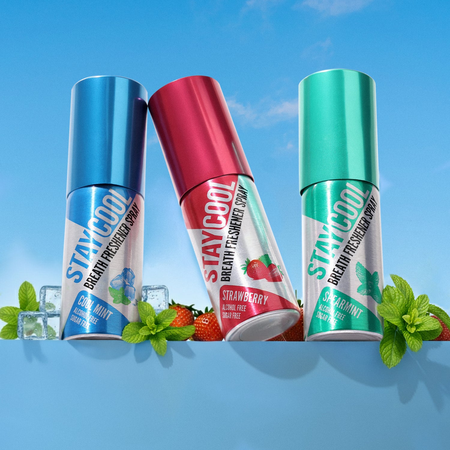 Three bottles of Stay Cool breath freshener spray with strawberries, mint leaves, and ice cube on a blue surface with a clear sky background.